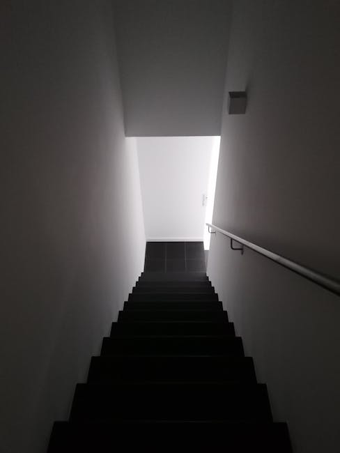 Inside a residential property, a professional removal team from manwithvanbethnalgreen.co.uk is engaged in loading furniture and boxes into a small, compact van parked just outside an entrance with a